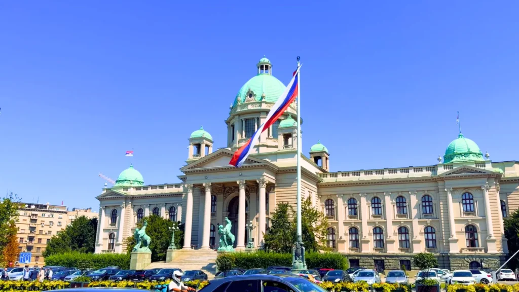 House of the National Assembly of Serbia in Belgrade, with green copper domes and the Serbian flag on a sunny day Belgrade Itinerary: National Assembly Building in the City Center